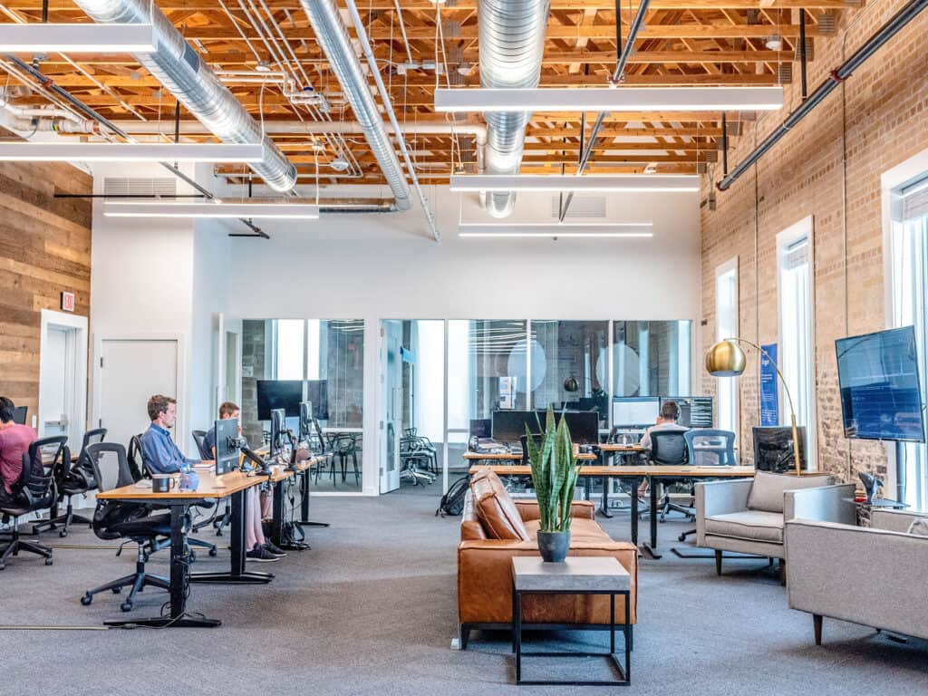 Modern open-plan office with exposed ceilings, a mix of desks, and a cozy seating area.