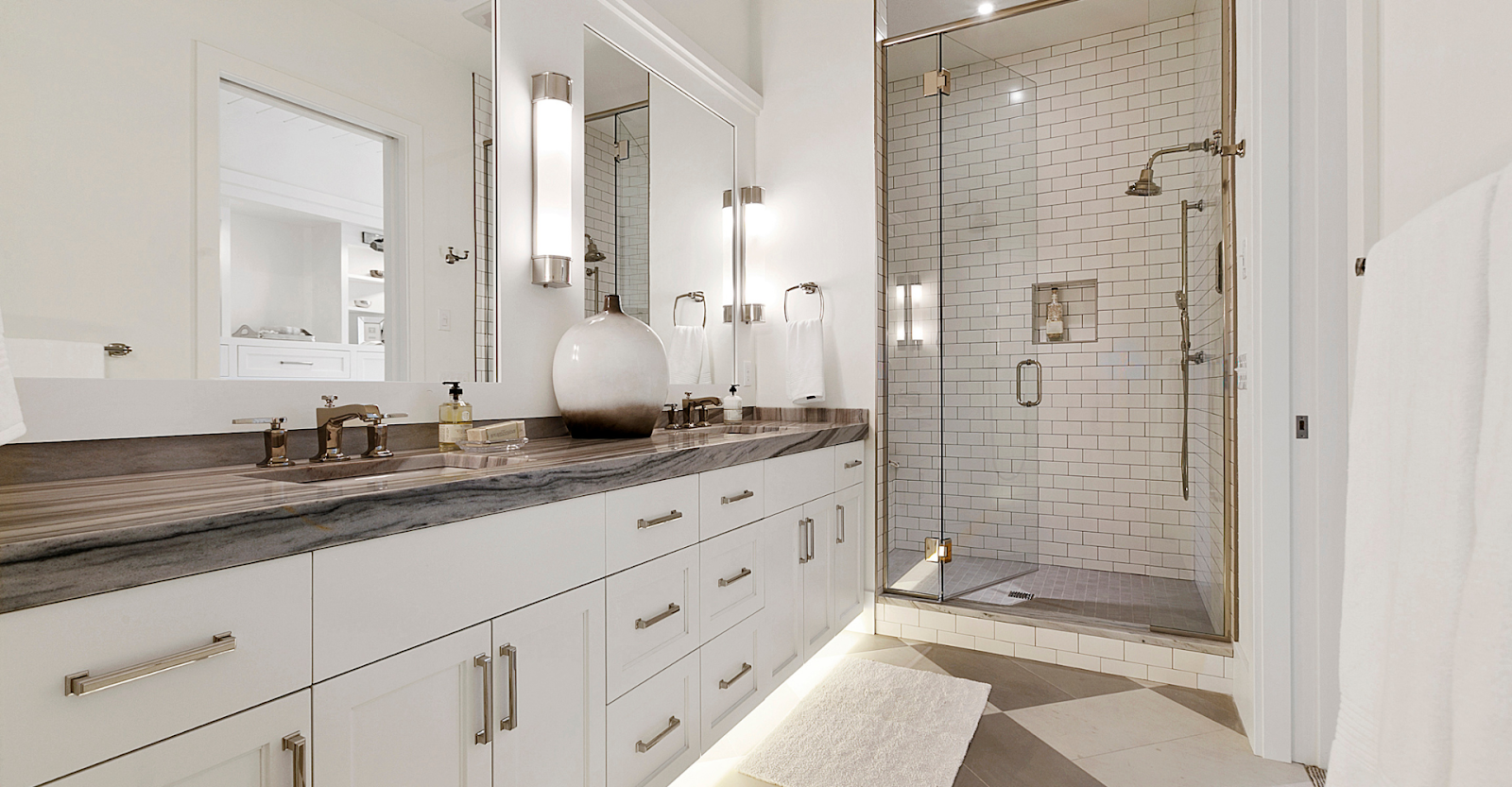 Modern luxury bathroom with a double vanity, sleek fixtures, and a glass-enclosed shower with white subway tiles.