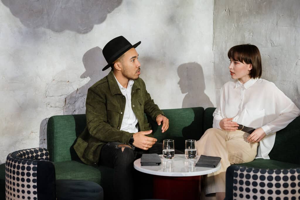 Two people engaged in conversation in a stylish cafe with green seating and modern decor.